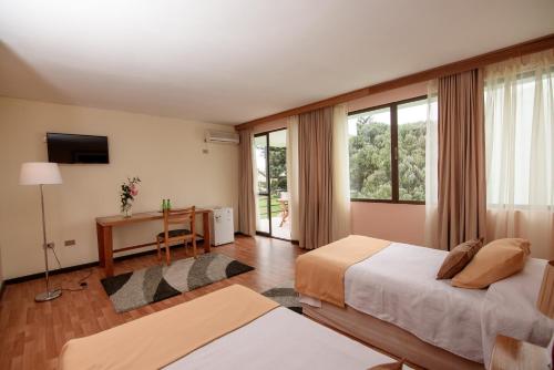 アリカにあるHotel del Valle Azapaのベッドルーム1室(ベッド2台、デスク、窓付)
