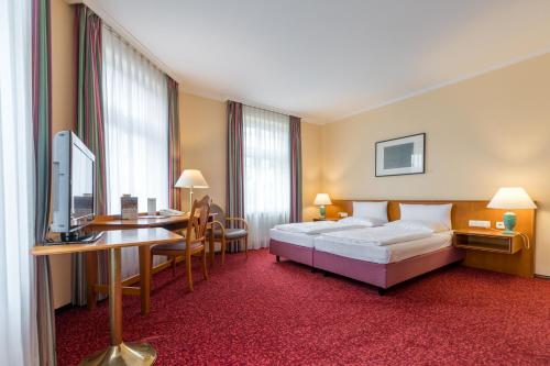 a hotel room with two beds and a desk and a television at Galerie Hotel Leipziger Hof in Leipzig