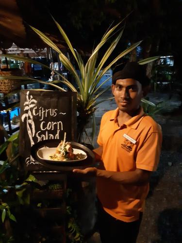 a man holding a plate of food next to a sign at Mutiara Beach Resort in Berakit
