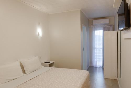 a white bedroom with a bed and a window at Pousada das Flores UpSerra in Urubici