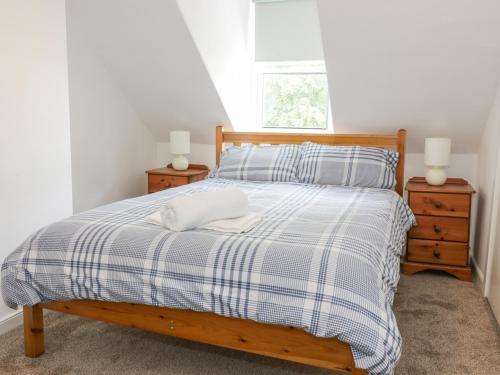 a bed with a blue and white plaid blanket and two night stands at Daisy Cottage in Moffat