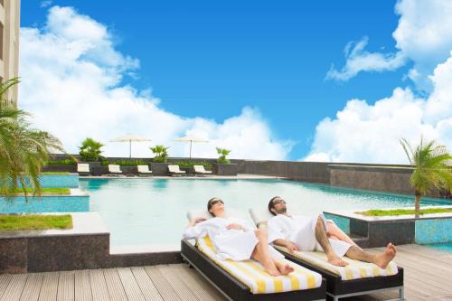 two men laying on beds next to a swimming pool at Radisson Blu Hotel New Delhi Dwarka in New Delhi
