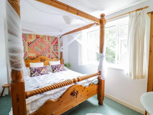 a bedroom with a wooden canopy bed with a window at Dyfi Cottage in Machynlleth
