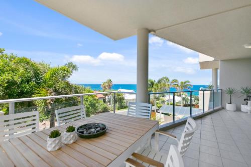 Un balcón con una mesa de madera y sillas y el océano. en Sunny and spacious Sunshine Beach, en Sunshine Beach