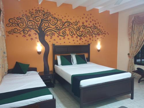 a bedroom with two beds with a tree mural on the wall at Hotel Eden Garden in Sigiriya