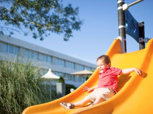 a young child sliding down a slide at a playground at Novotel Le Mans in Le Mans