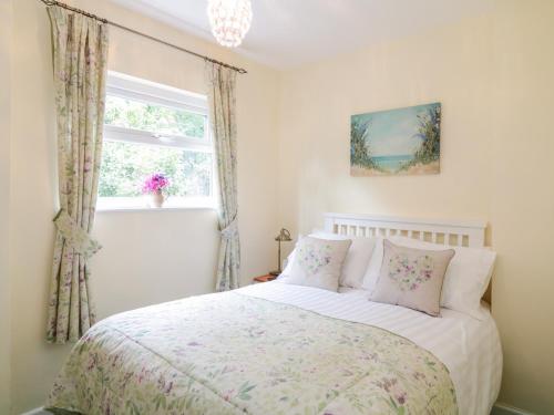 Un dormitorio con una cama con almohadas rosas y una ventana en The Roost en Camborne