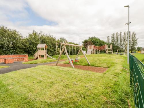 Un patio de juegos con un columpio de madera en un parque en Cherry Tree Cottage, en Ballintober