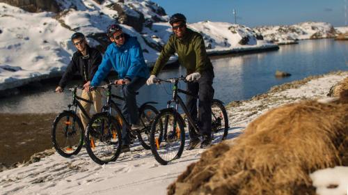 three people riding bikes in the snow next to a lake at HOTEL SØMA Sisimiut in Sisimiut