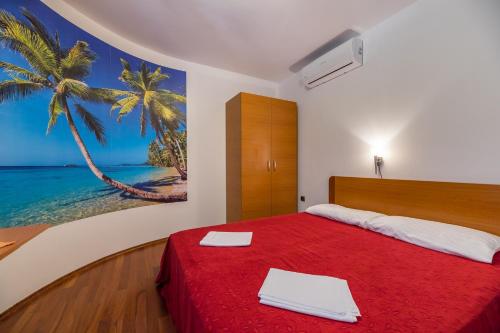 a bedroom with a red bed with a painting of a palm tree at Apartments Nada in Baška
