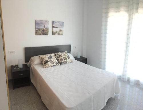 um quarto branco com uma cama com duas mesas de cabeceira e duas fotografias em Apartamento de una habitación em Málaga