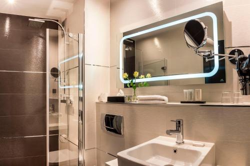 ein Bad mit einem Waschbecken, einem Spiegel und einer Dusche in der Unterkunft Boutique Hotel Poppenbütteler Hof in Hamburg