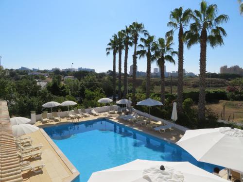 uma piscina com cadeiras e guarda-sóis e palmeiras em Villa Alcaide em Portimão