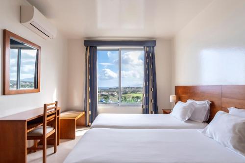 a hotel room with a bed and a desk and a window at Acorsonho Apartamentos Turisticos in Capelas