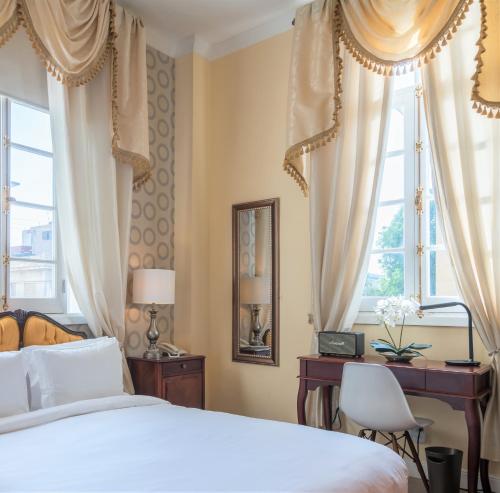 a bedroom with a bed and a desk and windows at El Candil Boutique Hotel in Havana