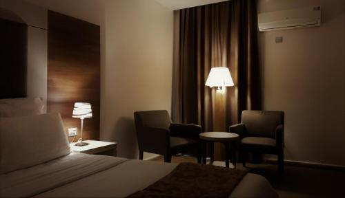 ein Hotelzimmer mit einem Bett, 2 Stühlen und einem Tisch in der Unterkunft Grand Hotel Central Conakry in Conakry