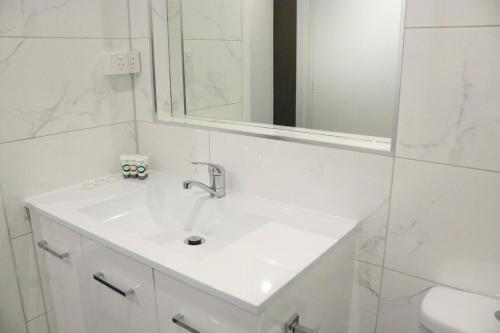 a white bathroom with a sink and a mirror at The Sands Motel Adelaide in Adelaide