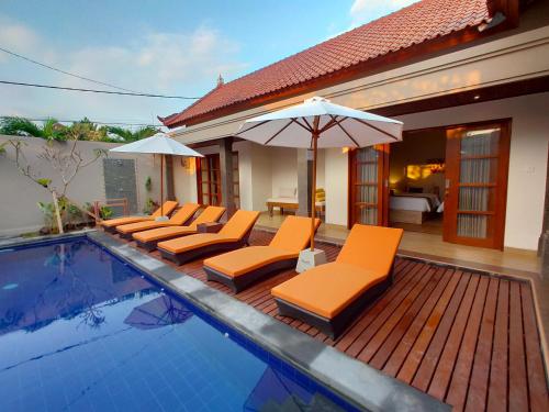 a pool with orange lounge chairs and an umbrella at Taman Amertha Villas by Maha Bali in Seminyak
