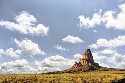 a mountain in the middle of a field with clouds at Kayenta Monument Valley Inn in Kayenta