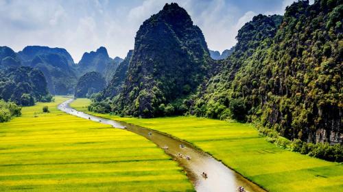 a river in a field with mountains in the background at Tam Coc Holiday Hotel & Villa in Ninh Binh