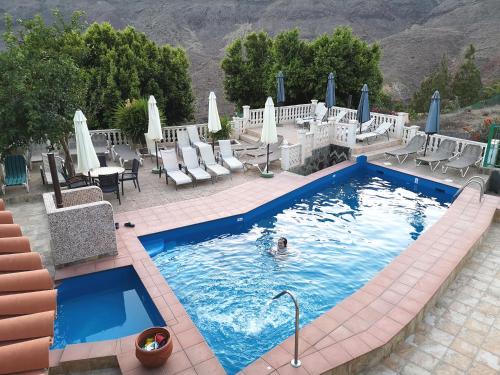 a person in a swimming pool with chairs and umbrellas at Finca Tomás y Puri in Fátaga