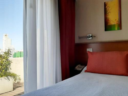 a bedroom with a bed with a red pillow and a window at Hotel Benevento in La Plata