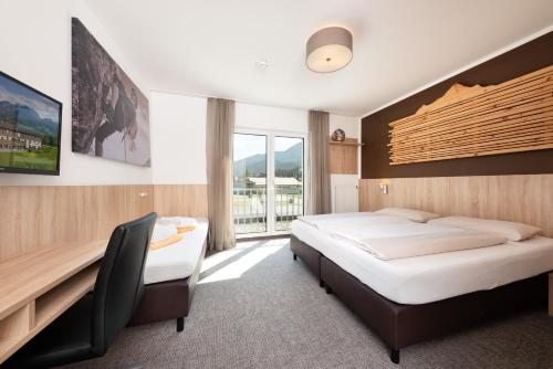 a bedroom with two beds and a desk and a window at Fairhotel Hochfilzen B&B in Hochfilzen