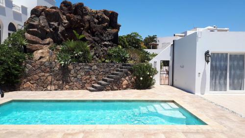 una piscina frente a una casa con pared de roca en Villa Essence - a unique detached villa with heated private pool, hottub, gardens, patios and stunning views! en Tías
