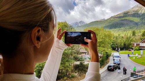 a woman taking a picture of the mountains with her cell phone at Studio Hrebienok 212 in Smokovce