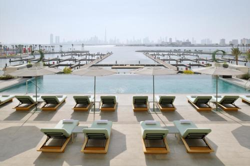 Vida Creek Harbour في دبي: مجموعة من الكراسي والمظلات بجانب المسبح