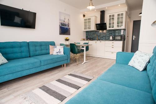 a living room with two blue couches and a kitchen at Zielona Przystań in Mechelinki