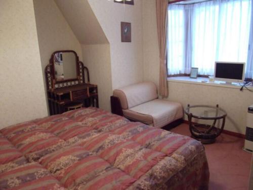um quarto com uma cama, uma cadeira e uma janela em Pension Bonnard em Hakuba