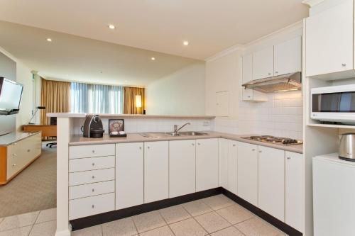 a white kitchen with a sink and a microwave at Rydges Darling Square Apartment Hotel in Sydney