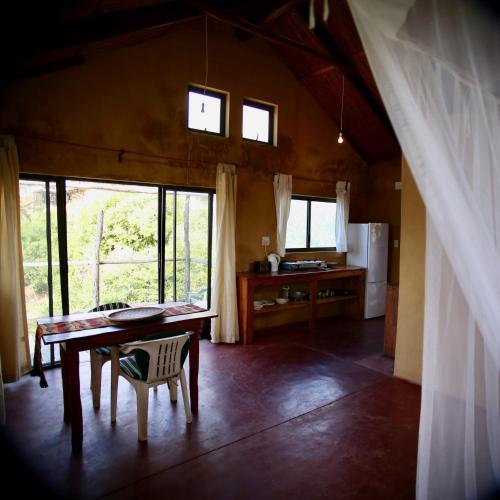 a room with a table and a kitchen with windows at Tree House Cottage, Garden View in Praia do Tofo