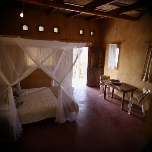 a bedroom with a canopy bed and a table at Tree House Cottage, Ocean View in Praia do Tofo