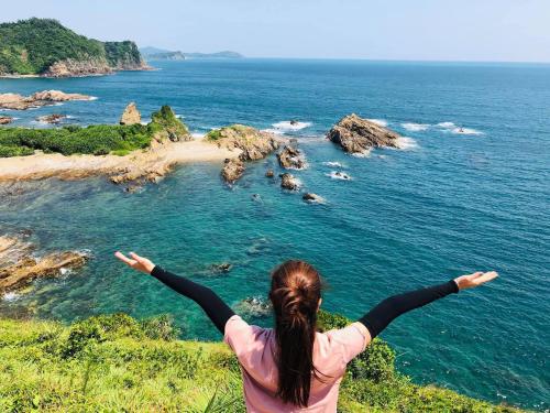 a woman standing on a hill with her arms outstretched looking at the ocean at Coto Center Homestay in Dao Co To