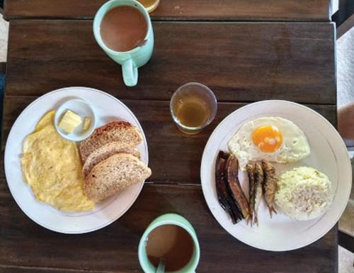 a wooden table with two plates of breakfast foods and coffee at Seaslugs Travellers Inn in El Nido