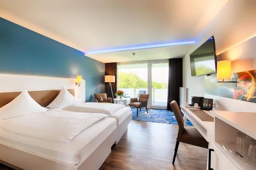 ein Hotelzimmer mit einem großen weißen Bett und einem Schreibtisch in der Unterkunft Seehotel am Stausee in Gerolstein