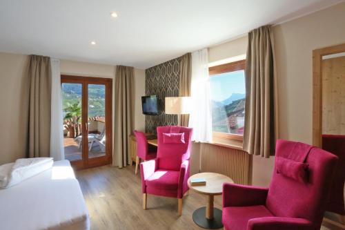 Habitación de hotel con sillas rosas, cama y ventana en Hotel Hofer, en Tirolo