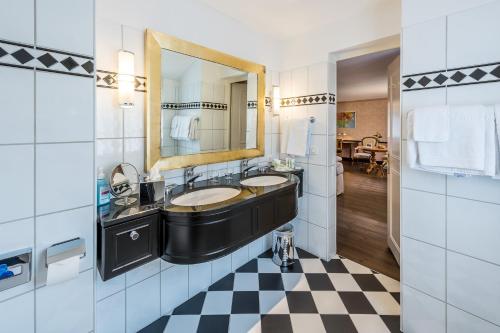 ein Badezimmer mit zwei Waschbecken, einem Spiegel und einem karierten Boden in der Unterkunft Kurhotel Im Park in Schinznach Bad