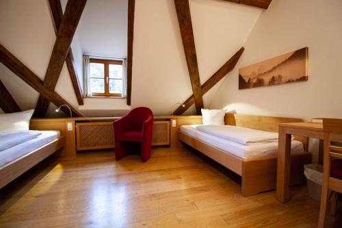 een kamer met 2 bedden en een rode stoel bij Gästehaus St. Georg - Weltenburger Klosterbetriebe GmbH in Kelheim