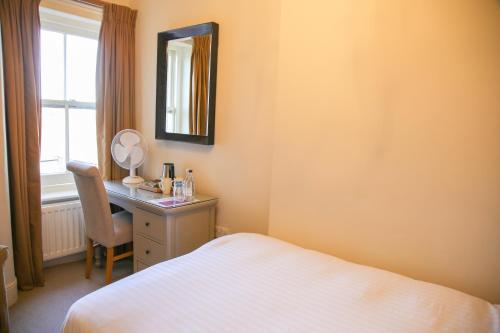 a bedroom with a bed and a desk with a mirror at The Bell Hotel in Sandwich