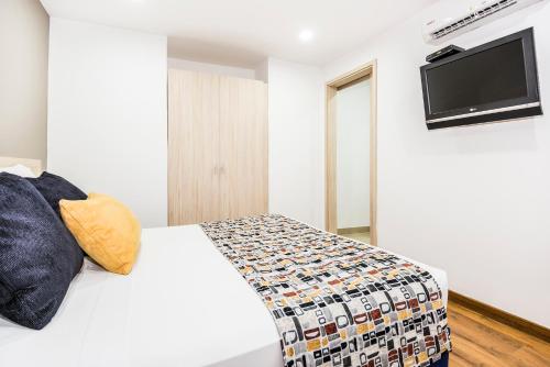 a bedroom with a white bed and a flat screen tv at Hotel Asturias Medellin in Medellín