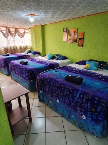 três camas num quarto com lençóis roxos em hotel kasa kamelot 2 em Quetzaltenango