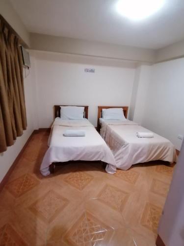 two beds in a room with white walls and wooden floors at Manora Apartment in Talisay