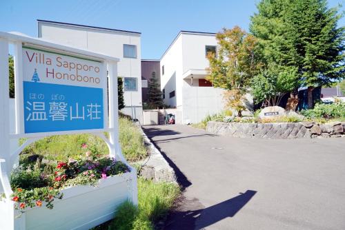 a sign in front of a building with flowers at Villa Sapporo Honobono in Sapporo