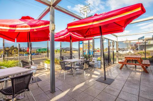 a patio with tables and chairs and red umbrellas at Nightcap at Riverside Hotel in Launceston