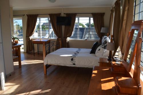 a bedroom with a bed and a desk and windows at Whale Tale in Cape Town