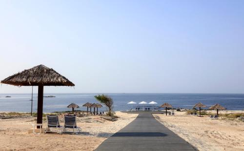 a boardwalk on a beach with umbrellas and chairs at Wyndham Garden Salalah Mirbat in Salalah