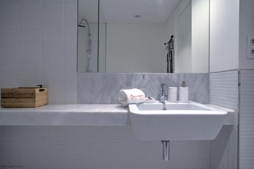 La salle de bains blanche est pourvue d'un lavabo et d'un miroir. dans l'établissement Urban Beach Estoril Apartment, à Estoril